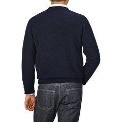 A person wearing a William Lockie Oxford Blue Deep V-Neck Lambswool Sweater and blue jeans is shown from behind against a plain background.