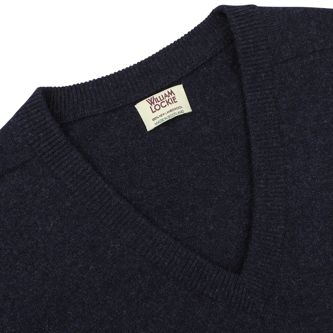 A close-up of an oxford blue, deep v-neck sweater with a tag reading "William Lockie, Scottish Made, Lambswool" near the neckline.