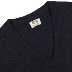 A close-up of an oxford blue, deep v-neck sweater with a tag reading "William Lockie, Scottish Made, Lambswool" near the neckline.