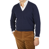 A man wearing a William Lockie Oxford Blue Deep V-Neck Lambswool Sweater and brown pants.
