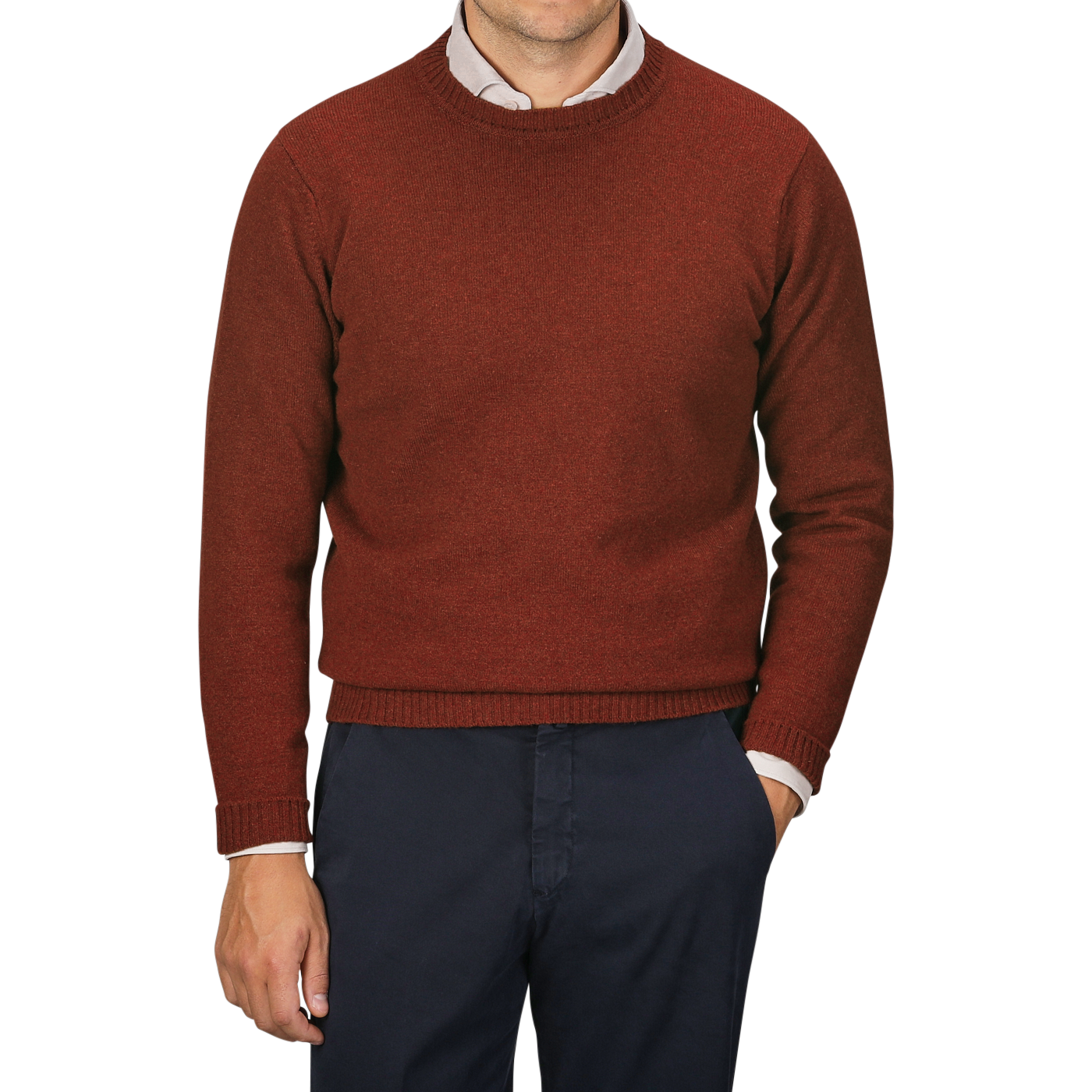 A person wearing a William Lockie Sienna Brown Crew Neck Lambswool Sweater over a white collared shirt pairs them with dark trousers, standing in front of a plain, light grey background.