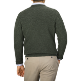 A person wearing a William Lockie Spruce Green Shetland Lambswool V-Neck Sweater over a collared shirt and light beige pants, seen from the back.