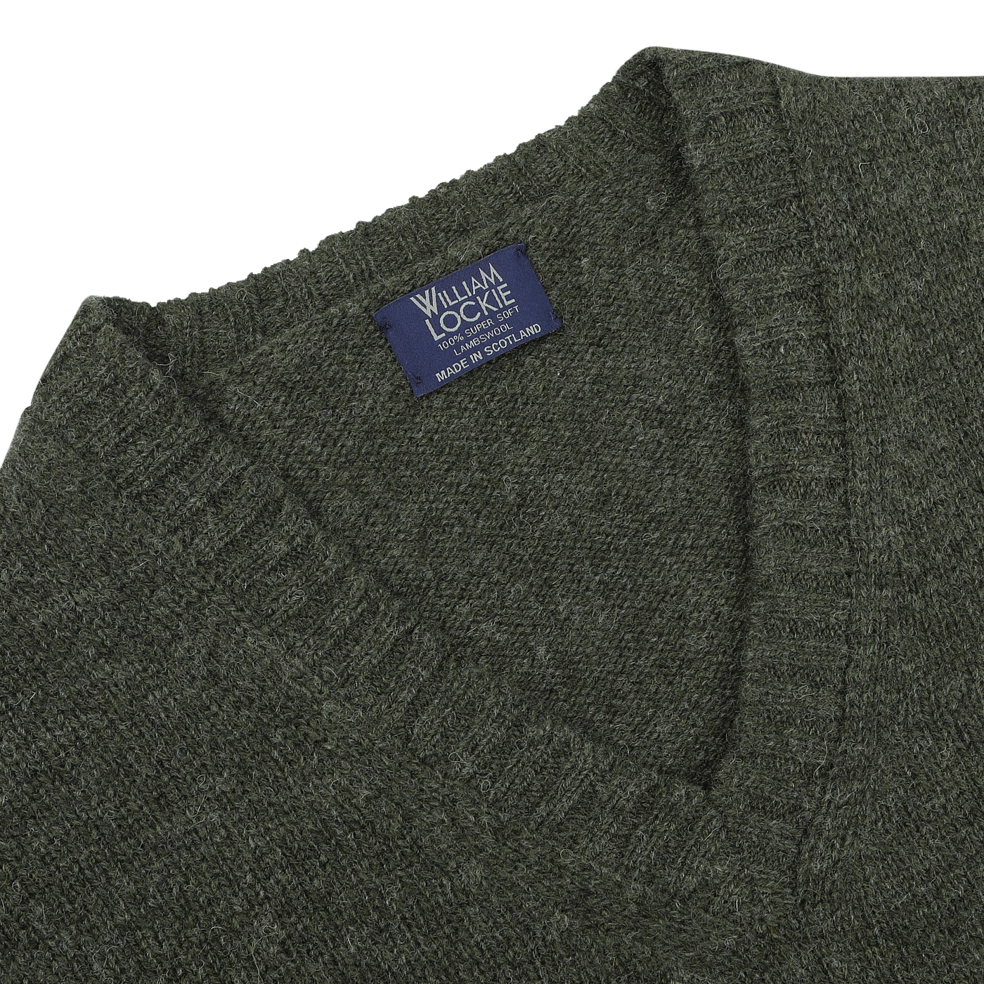 Close-up image of a seasonal William Lockie Spruce Green Shetland Lambswool V-Neck Sweater with a label that reads "Made in Scotland.