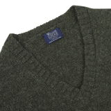 Close-up image of a seasonal William Lockie Spruce Green Shetland Lambswool V-Neck Sweater with a label that reads "Made in Scotland.