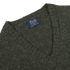 A close-up of the luxurious Spruce Brushed Wool Shetland Lambswool V-Neck sweater, showcasing its exquisite spruce green hue and a "William Lockie" label that proudly declares it is made in Scotland.