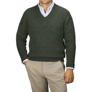 A person is shown from the chest down, wearing a Spruce Green Shetland Lambswool V-Neck Sweater by William Lockie over a light blue collared shirt and beige pants.