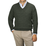 A person is shown from the chest down, wearing a Spruce Green Shetland Lambswool V-Neck Sweater by William Lockie over a light blue collared shirt and beige pants.