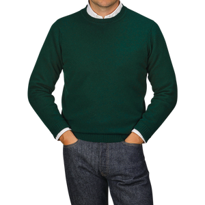 A person in a Tartan Green Crew Neck Lambswool Sweater from William Lockie and blue jeans stands with their hands in their pockets. The face is not visible.