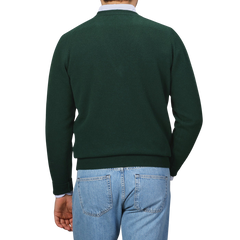 A person wearing a Tartan Green Deep V-Neck Lambswool Sweater by William Lockie and light blue jeans is standing with their back to the camera against a neutral background.