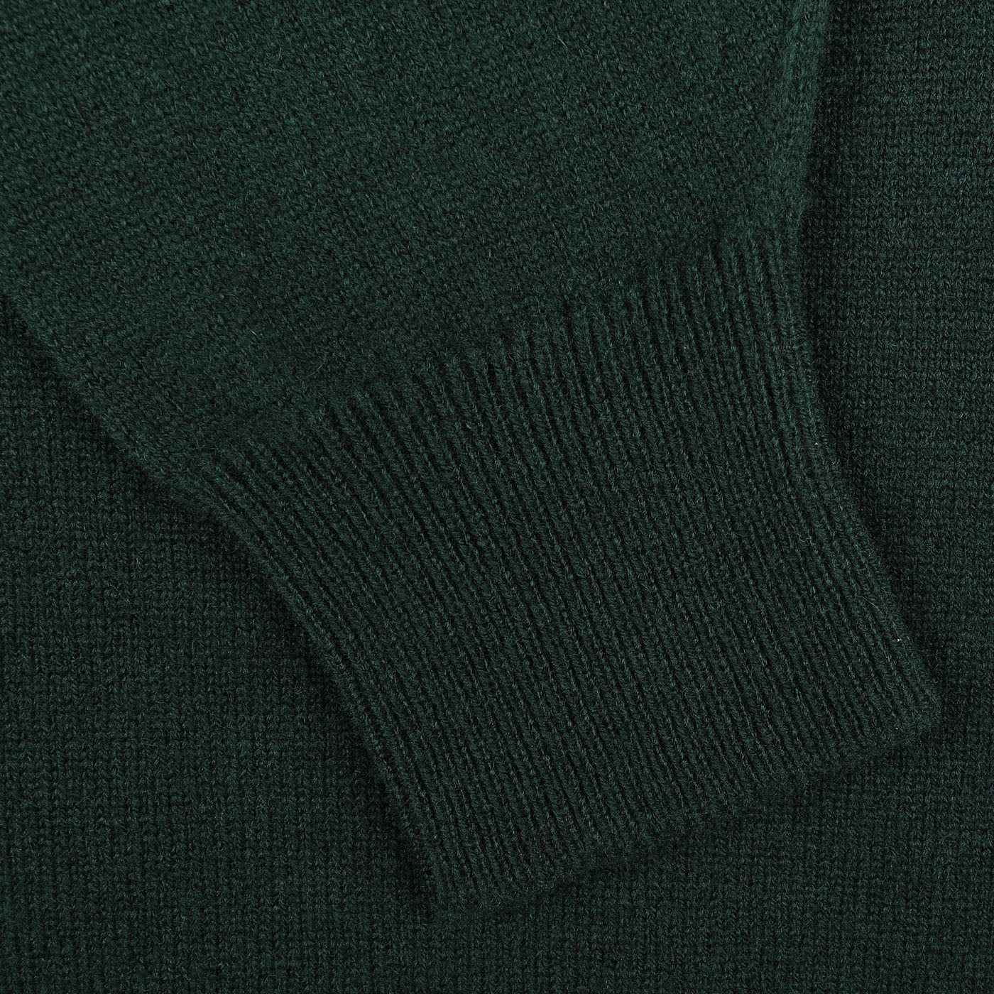 A close-up of the sleeve from the Tartan Green Deep V-Neck Lambswool Sweater by William Lockie reveals ribbed knitting at the cuff and a smooth texture on the main fabric, highlighting its exquisite craftsmanship.