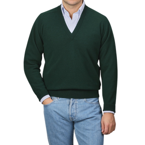 A person in a William Lockie Tartan Green Deep V-Neck Lambswool Sweater and blue jeans stands against a plain background.