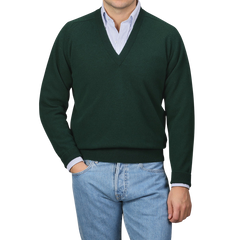 A person in a William Lockie Tartan Green Deep V-Neck Lambswool Sweater and blue jeans stands against a plain background.