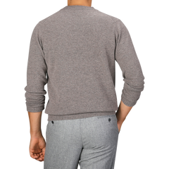 A person wearing a beige Scottish lambswool sweater and grey pants is photographed from behind. The William Lockie Vole Beige Crew Neck Lambswool Sweater features long sleeves and a crew neck.