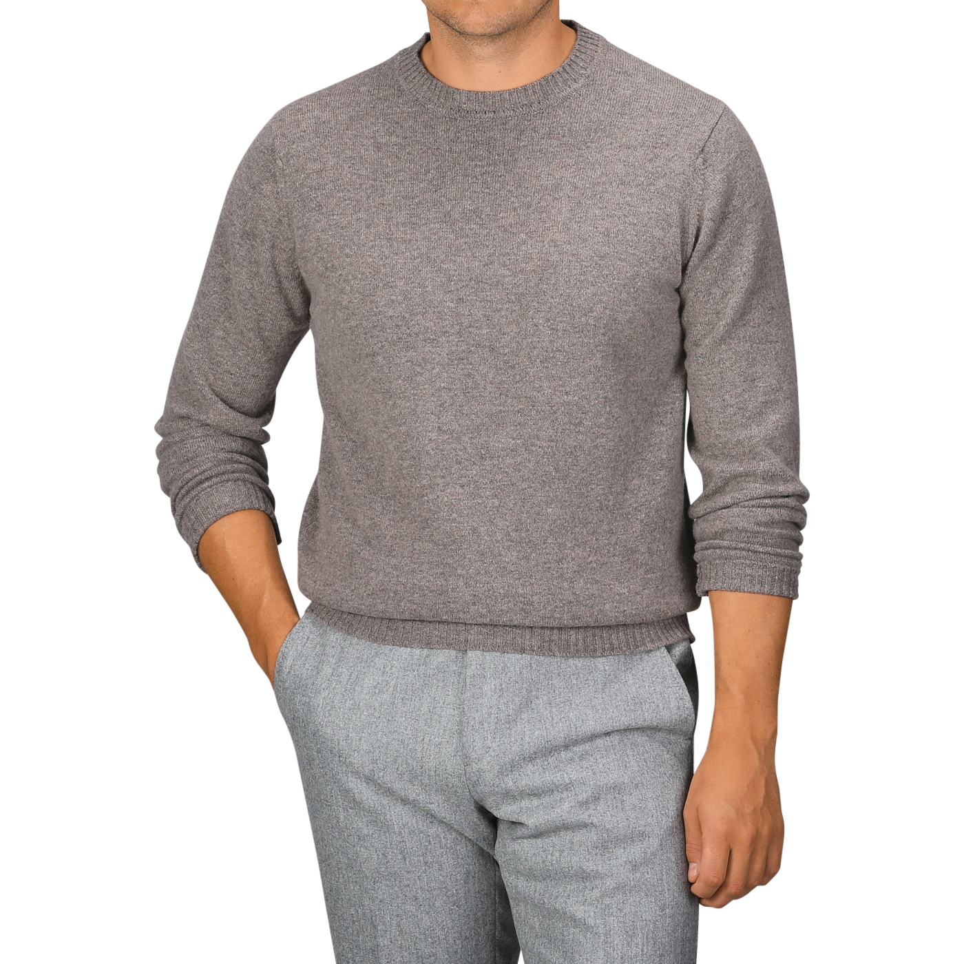 A person wearing a William Lockie Vole Beige Crew Neck Lambswool Sweater and gray pants, standing with one hand in a pocket against a plain background.