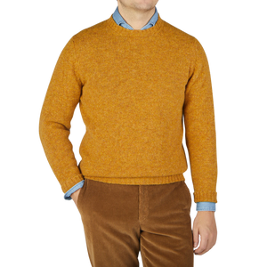 A man wearing a William Lockie Cumin Yellow Shetland Lambswool Crew Neck Sweater and brown pants.