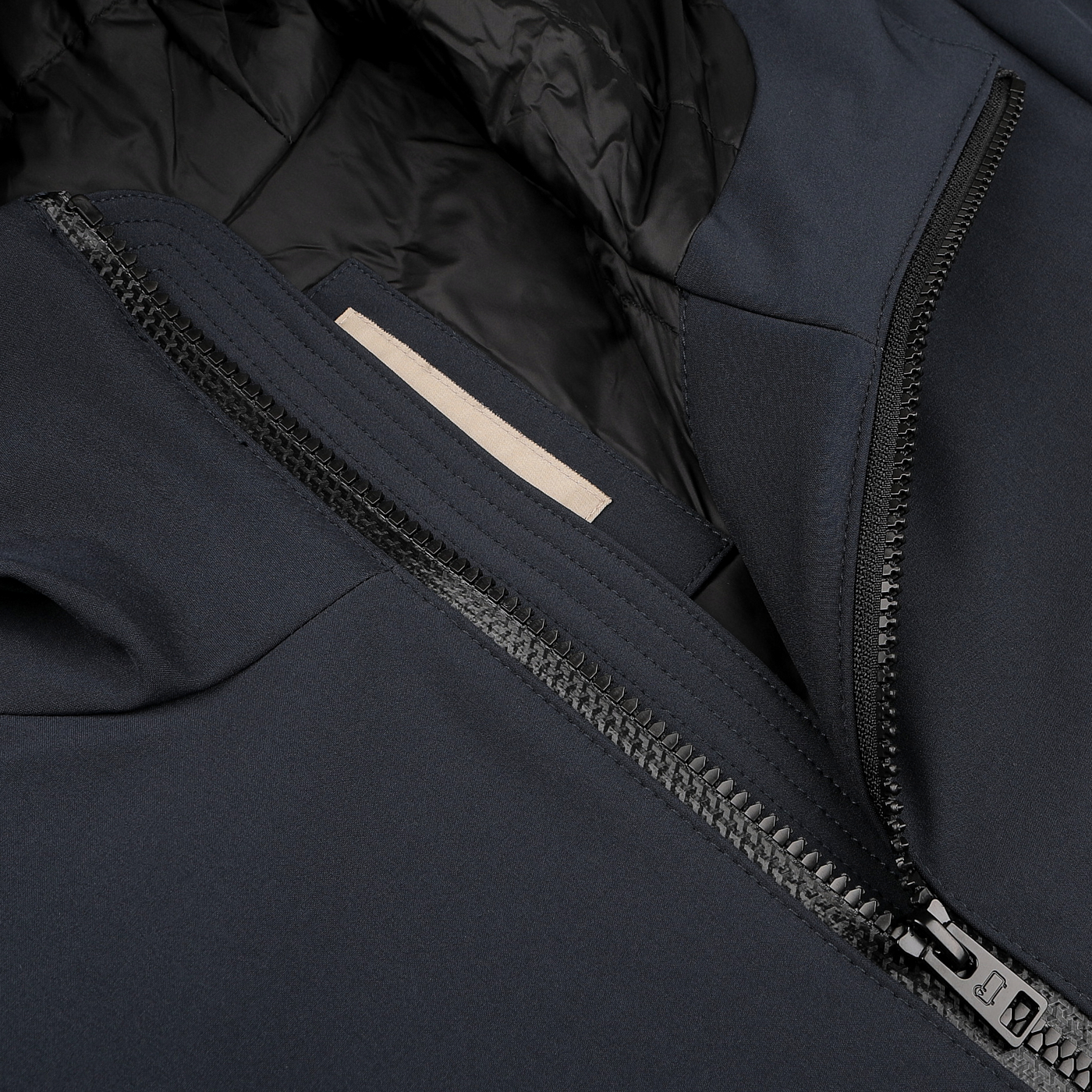 Close-up of a dark-colored Melton Blue Pacific Soft Shell Jacket by Woolrich, showcasing a partially open zipper that reveals the label inside.