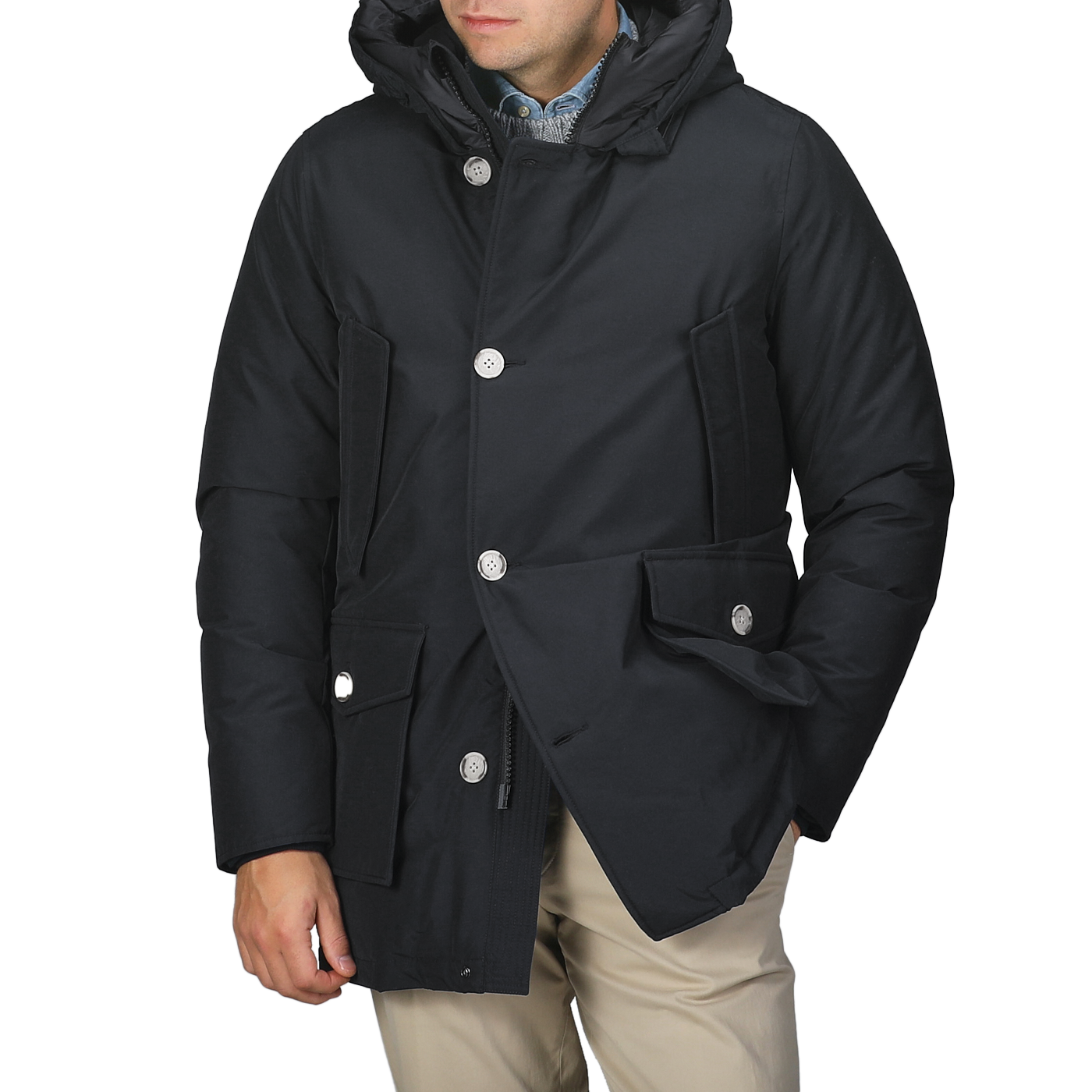 A person wearing a Melton Blue Stretch Nylon Arctic Parka by Woolrich, made from waterproof stretch nylon with button closures and large pockets, stands against a neutral background.