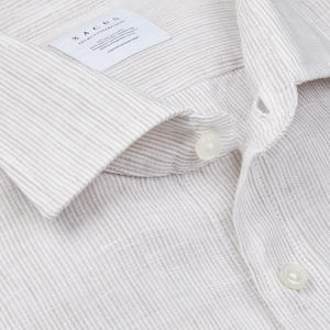 Close-up of a beige striped washed linen Legacy shirt with buttons and a collar displaying a label with the Xacus brand name.