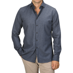 A man wearing a long-sleeved, seasonal Blue Melange Cotton Flannel Tailor Fit Shirt by Xacus and beige pants stands with one hand in his pocket. His head is cropped out of the image.