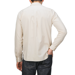 A person in a Cream Beige Cotton Twill Legacy Shirt by Xacus and dark jeans, seen from behind, casually slips one hand into their pocket.