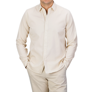 An individual dressed in the Cream Beige Cotton Twill Legacy Shirt by Xacus stands with hands tucked into their pockets. The backdrop features a neutral gray hue.