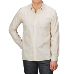 A man in an Xacus Cream Beige Cotton Twill Legacy Shirt and dark jeans stands against a neutral background, one hand in his pocket.