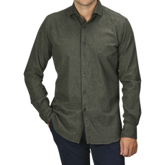 A person is standing with one hand in their pocket, wearing a Xacus Green Melange Cotton Flannel Tailor Fit Shirt and slim fit dark pants against a plain, light gray background. The person's face is not visible.