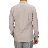 A person wearing a long-sleeved, light beige cotton flannel tailor fit shirt from Xacus and gray pants, photographed from the back against a gray background.