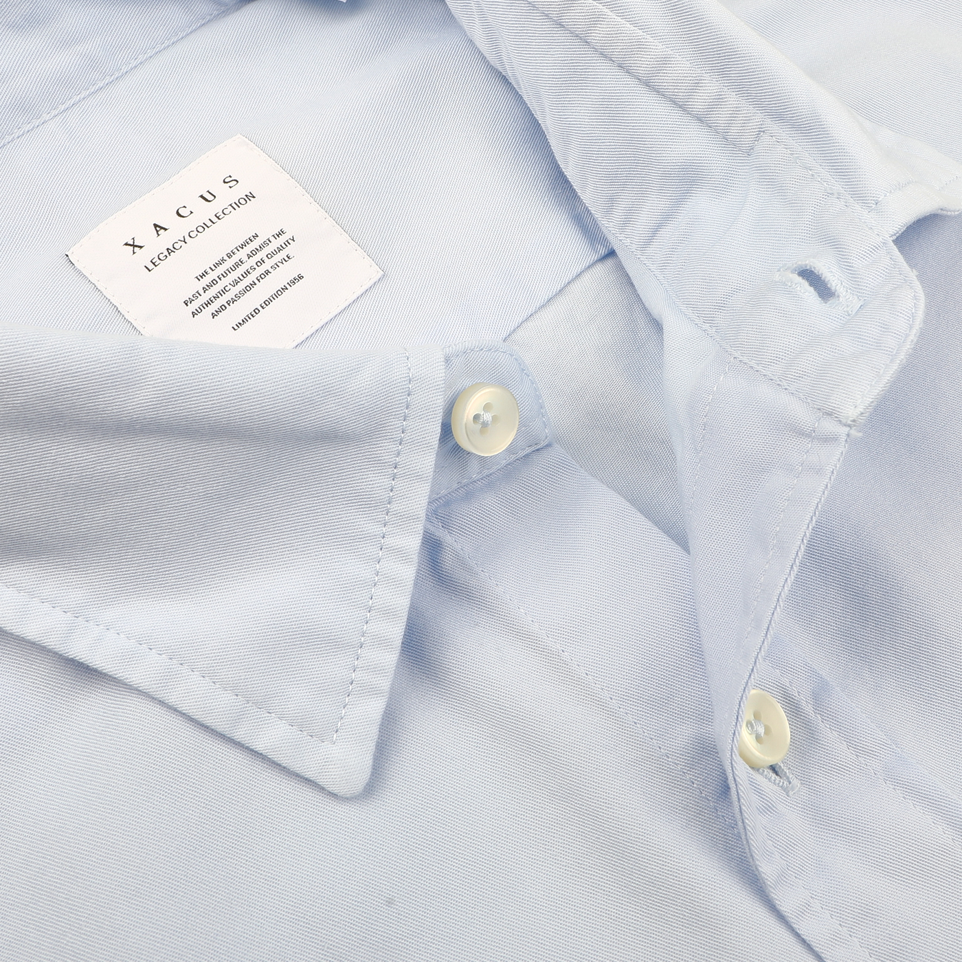 Close-up of the Light Blue Cotton Twill Legacy Shirt by Xacus, showcasing pure cotton fabric with an open collar and visible buttons. A label inside the collar reads "Xacus" with additional text in smaller font.