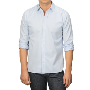 A person wearing an Xacus Light Blue Cotton Twill Legacy Shirt with rolled-up sleeves and dark jeans stands against a plain background.