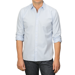 A person wearing an Xacus Light Blue Cotton Twill Legacy Shirt with rolled-up sleeves and dark jeans stands against a plain background.