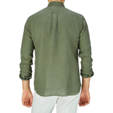 A person standing with their back to the camera, wearing an Xacus Olive Green Washed Linen Legacy Shirt with a cut-away collar and white pants.