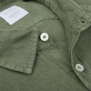Olive green casual shirt detail featuring a cut-away collar, button, and care label. 

becomes

Xacus Olive Green Washed Linen Legacy Shirt featuring a cut-away collar, button, and care label.