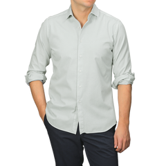 Dressed in a Sage Green Cotton Twill Tailor Fit Shirt with rolled sleeves by Xacus and dark trousers, a person stands against a neutral background.