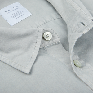 Close-up of a sage green, washed cotton twill Xacus shirt collar with a button and a label displaying the brand "yacq".