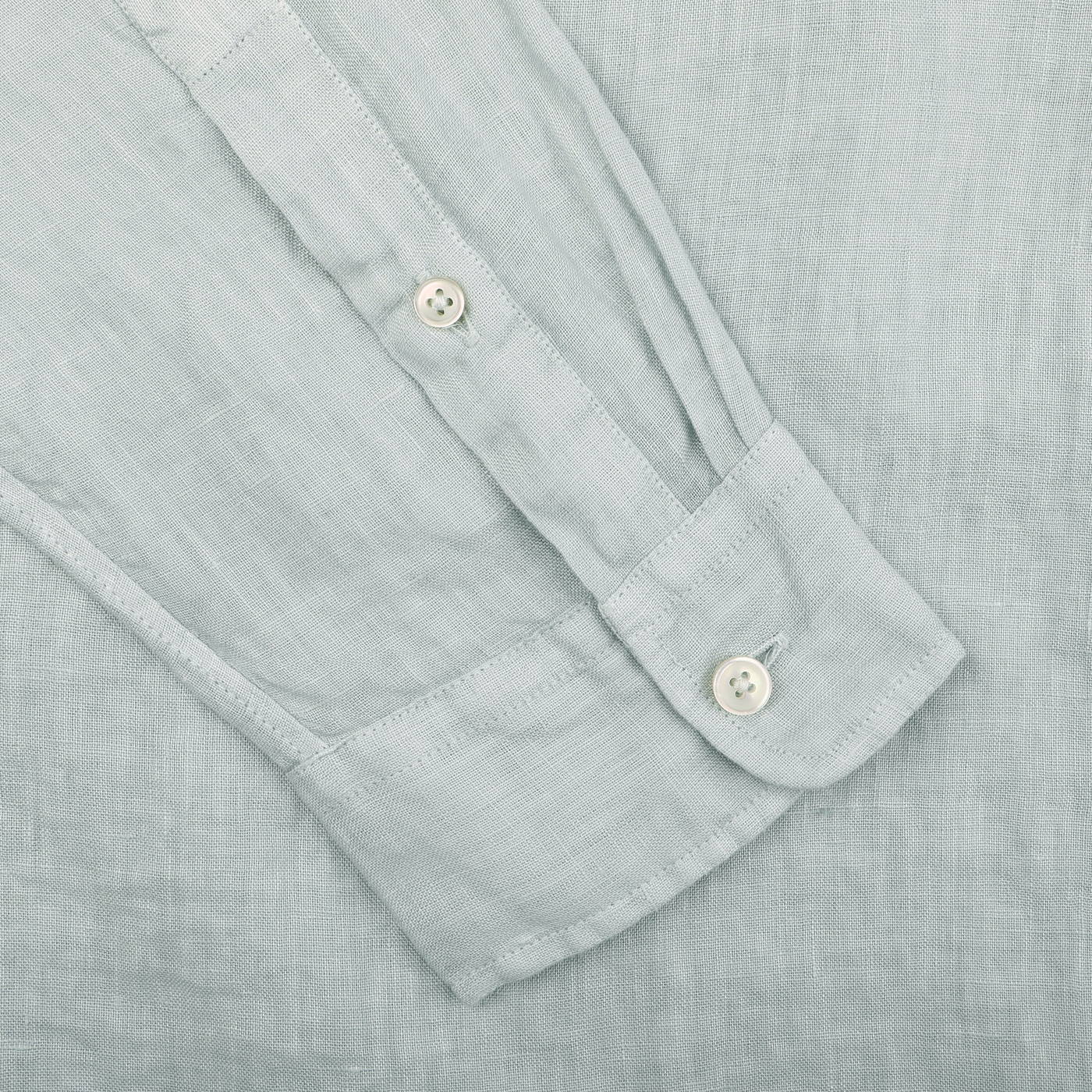 A close-up of the sleeve on the Sage Green Washed Linen Legacy Shirt by Xacus reveals two cuff buttons, highlighting its pure linen fabric's texture and intricate weave.