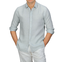 A person wearing the Xacus Sage Green Washed Linen Legacy Shirt with rolled-up sleeves and white pants, showcasing a stylish cut-away collar against a plain background.