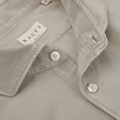 Close-up of a washed beige tailor fit collared shirt with white buttons and a tag reading "Xacus," crafted from pure cotton mussola.