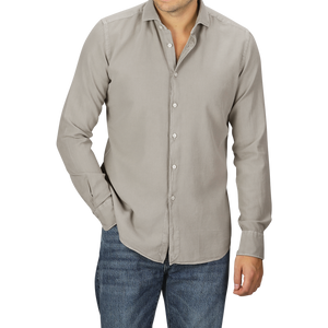 A person in a Washed Beige Mussola Cotton Tailor Fit Shirt by Xacus with the top button undone and slim fit blue jeans, posing with one hand in the pocket and the other by their side.