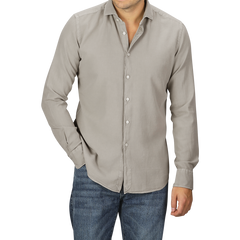 A person in a Washed Beige Mussola Cotton Tailor Fit Shirt by Xacus with the top button undone and slim fit blue jeans, posing with one hand in the pocket and the other by their side.