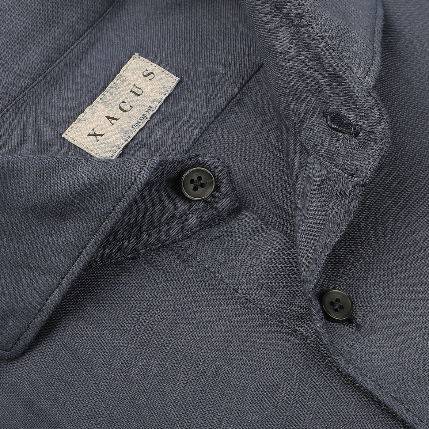 Close-up of a Washed Navy Mussola Cotton Tailor Fit Shirt with two black buttons and a label with the text "Xacus," crafted from pure cotton.