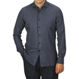 A man is wearing a Washed Navy Mussola Cotton Tailor Fit Shirt from Xacus. The pure cotton material and slim fit accentuate his frame as he stands with one hand in his pocket against a plain background. His face is not visible.