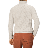 Rear view of a person wearing an Ecru Beige Wool Cable Knit Rollneck by Zanone and rust-colored pants, standing against a plain background.