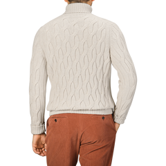 Rear view of a person wearing an Ecru Beige Wool Cable Knit Rollneck by Zanone and rust-colored pants, standing against a plain background.