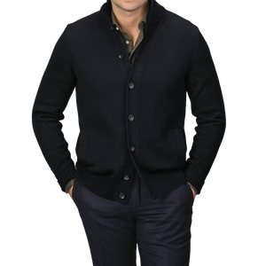 A person in a Zanone Navy Blue Merino Wool Button Cardigan, styled over a dark shirt and pants with hands casually tucked in pockets, stands against a gray background.