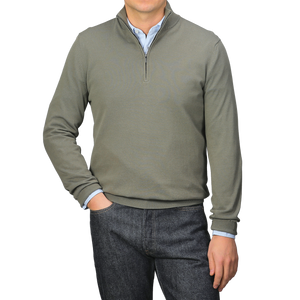 Dressed in an Olive Green Crepe Cotton 1/4 Zip Sweater by Zanone over a blue shirt and dark jeans, a person exudes effortless style, with one hand in their pocket while the other hangs by their side.