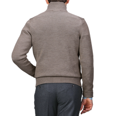 The individual, turned away from the camera, is dressed in a brown turtleneck sweater and gray pants, elegantly accessorized with a Taupe Beige Merino Wool Button Cardigan by Zanone.