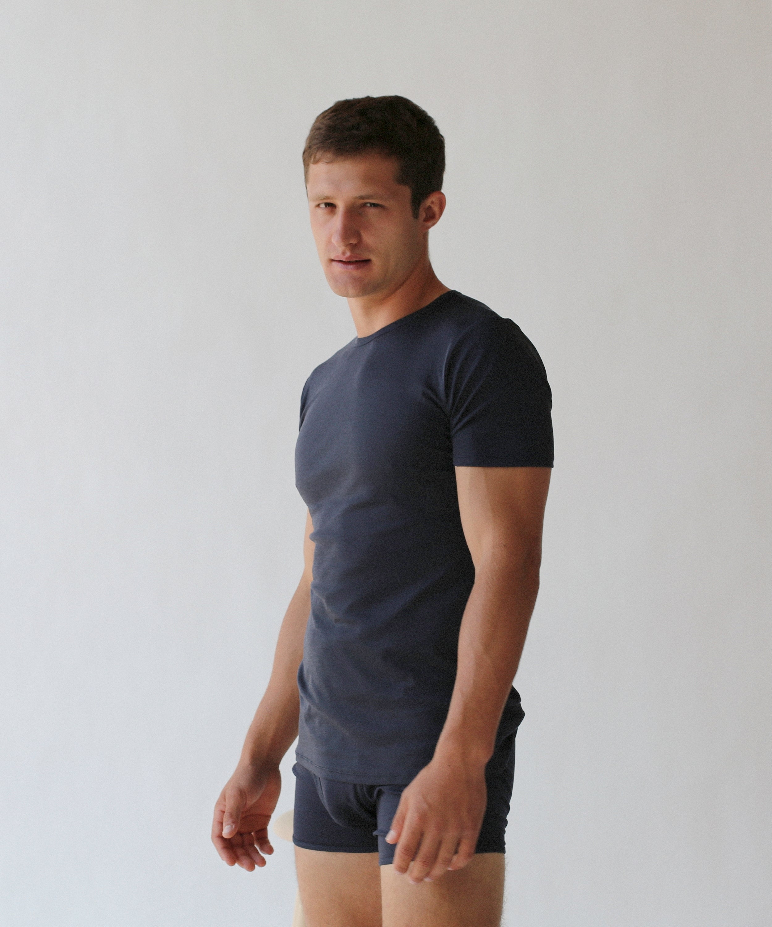 A man in a navy blue, slim fit ensemble featuring "The White Briefs" Earth Organic Pima Cotton Crewneck T-shirt and matching shorts stands against a plain white background.