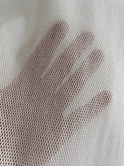 A hand is pressing against the white netted fabric of The White Briefs' Rye Organic Cotton Mesh Singlet, creating a visible impression through the pattern.