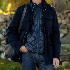 A person wearing a dark blue jacket over a Taion Navy Blue Nylon Down Padded Zip Vest, carrying a bag on their shoulder, stands outdoors.